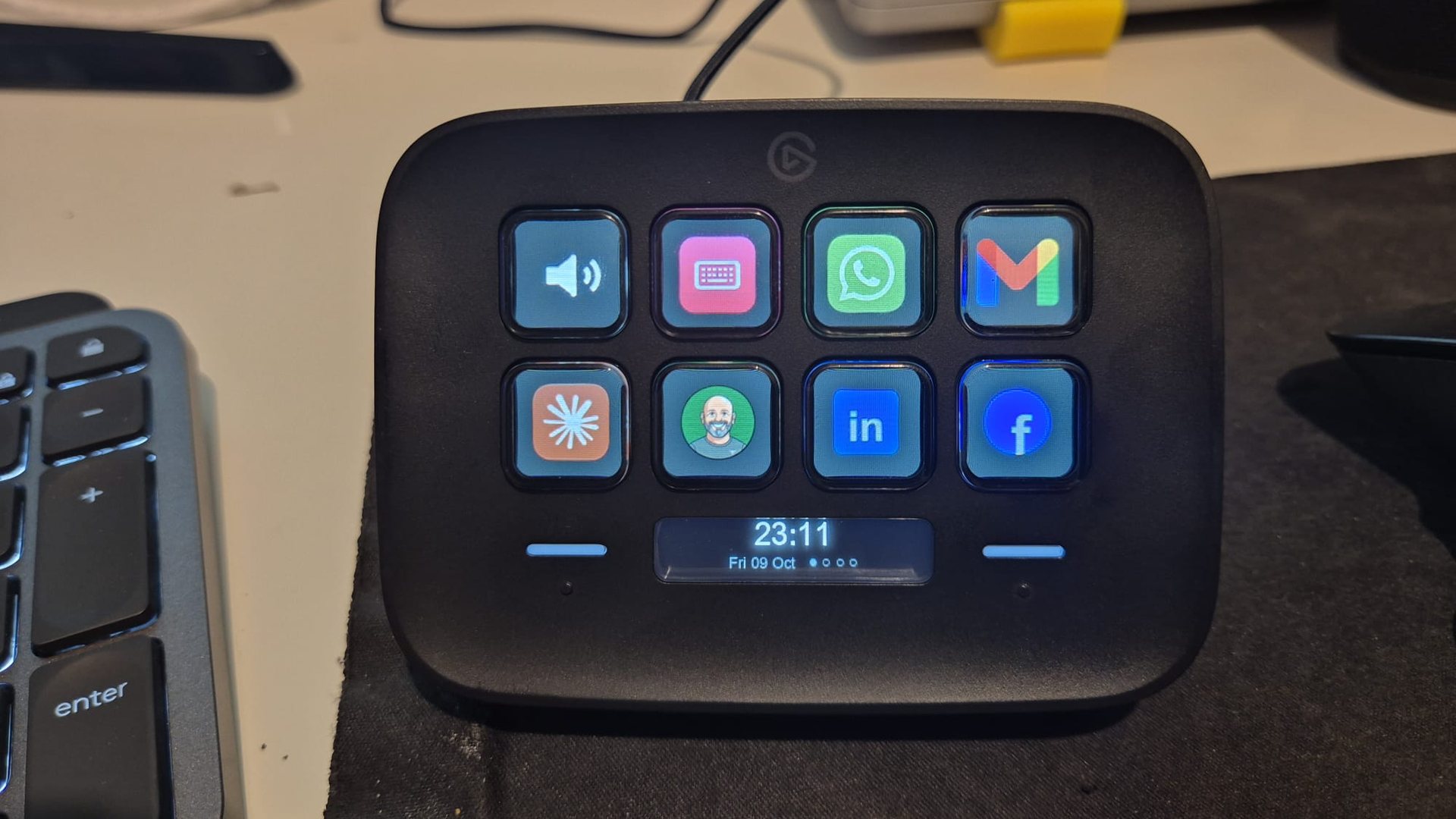 A Stream Deck Neo on a desk with icon keys and a clock on its display