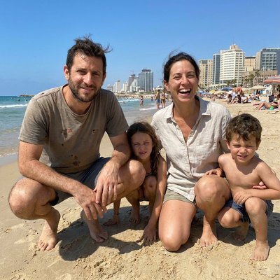 Generated photo of a man crouching on a Tel Aviv beach with his wife and two young children.